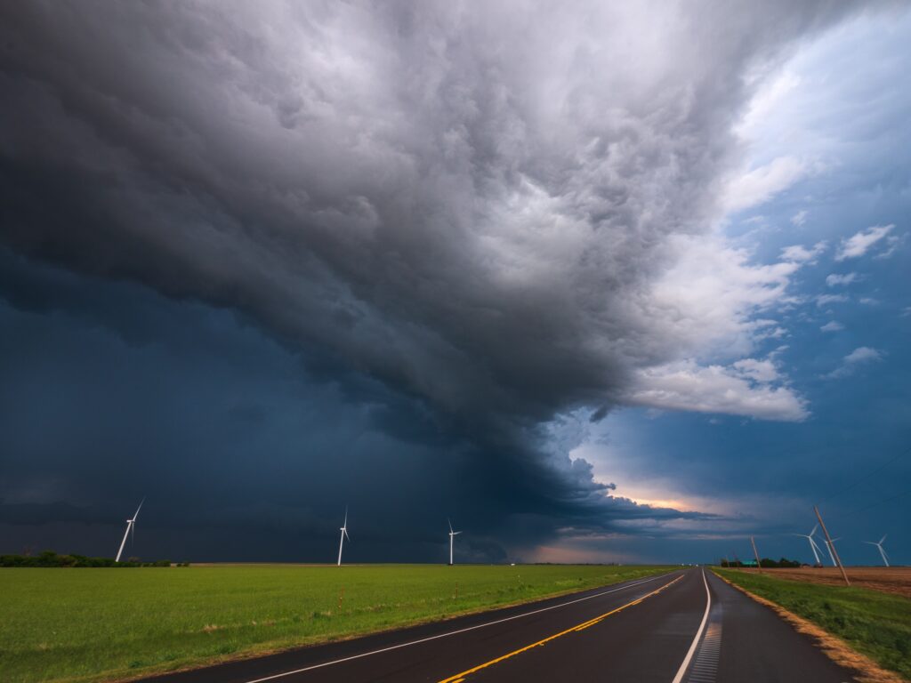 a photograph of a thunderstorm over a field and highway.