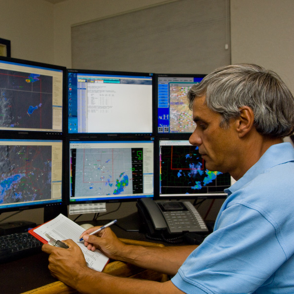 A meteorologist working in front of several computer monitors displaying weather data.