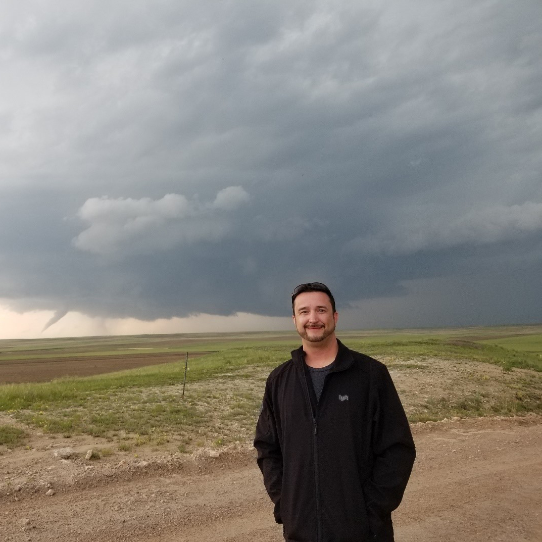 A Meteorologist standing in front of a tornado in a field.