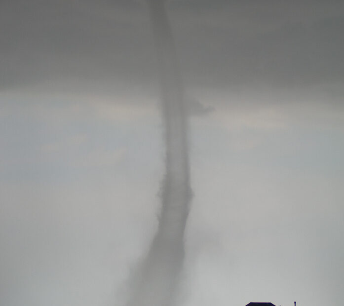 A photograph of a tornado and next to a house.