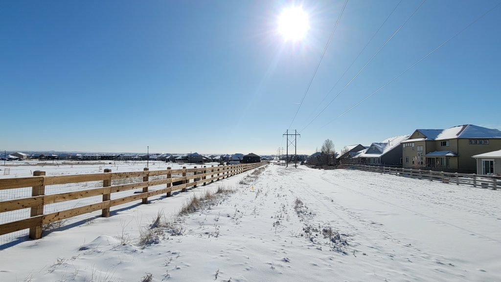 A photograph of a snow covered road with telephone poles and a wooden fence.