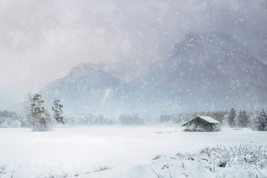 A picture of a high country cabin and forest next to a couple of mountains with a strong snow storm occurring.