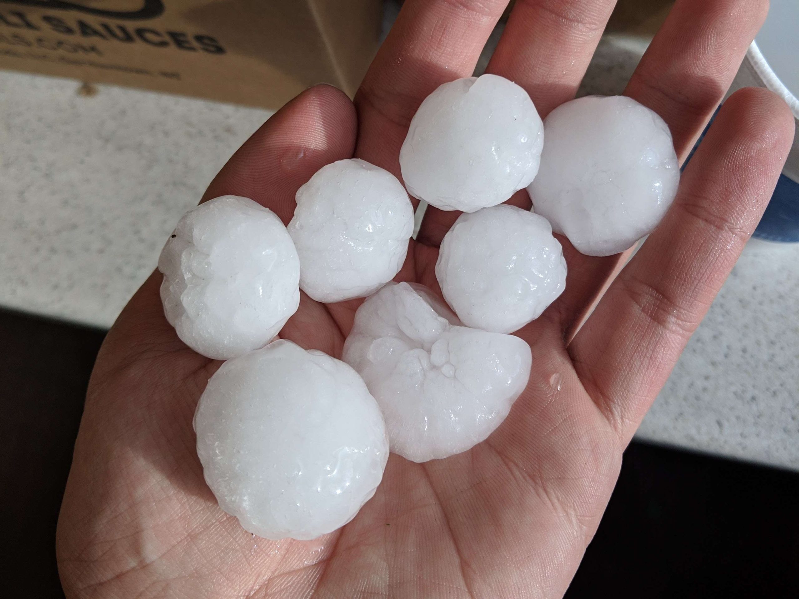 A photograph of ping-pong-ball-sized hail stones in someones hand.