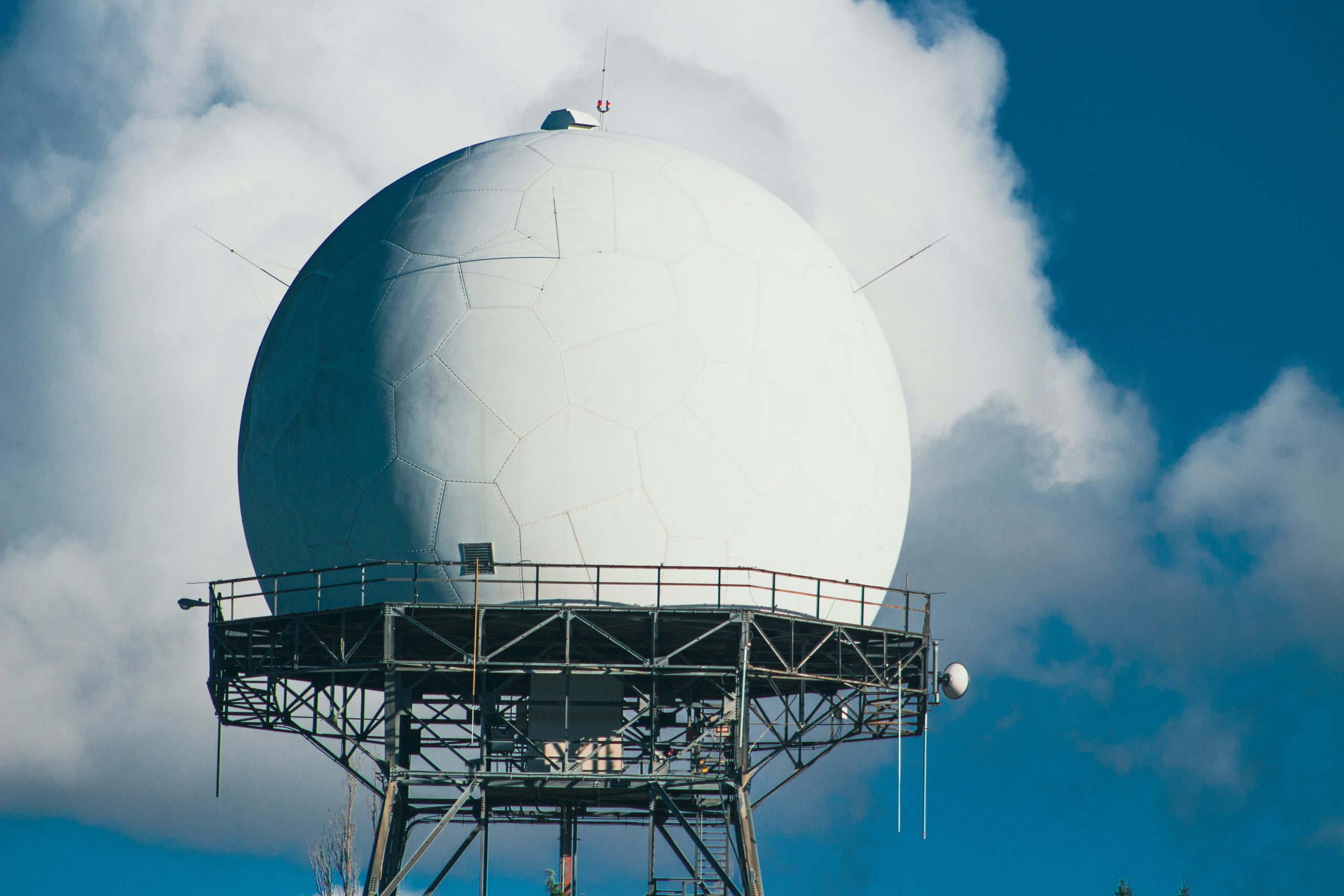 A radar dome on scaffolding against a blue sky with clouds.