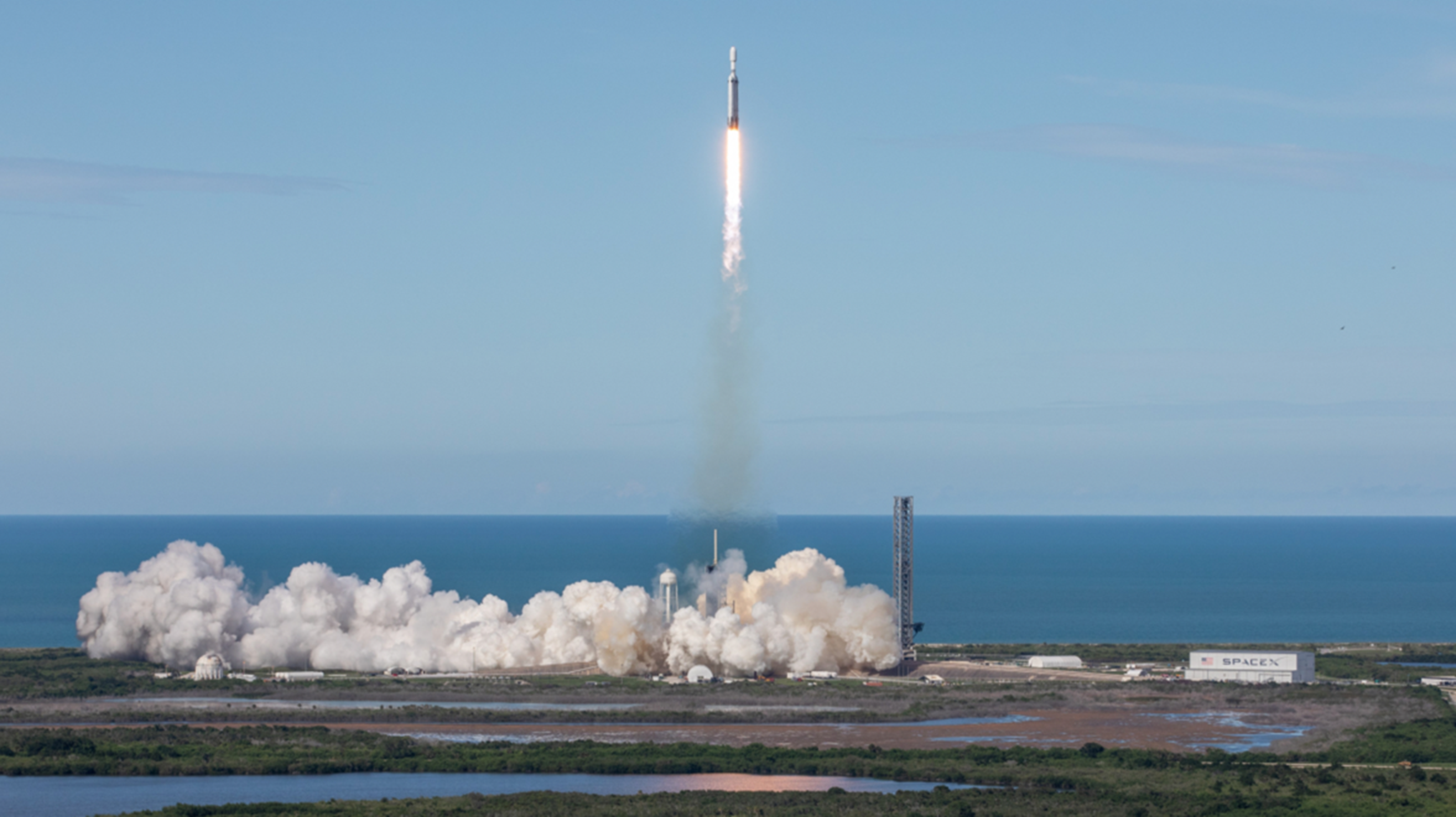 A photograph of a space shuttle launch in Florida next to wetlands with an ocean and blue clear skies in the background.